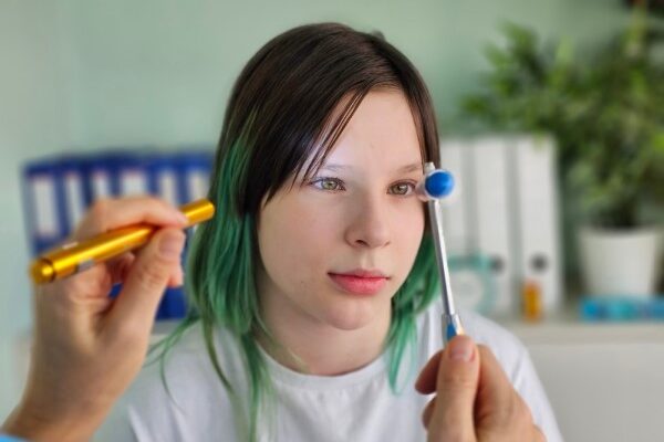 A neurologist checks the visual reflex of a teenage girl