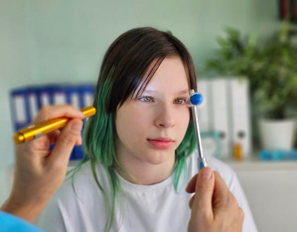 A neurologist checks the visual reflex of a teenage girl