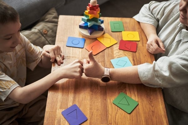 Learning Disabilities in New York A Child and an Adult Play a Hand Game at a Wooden Table