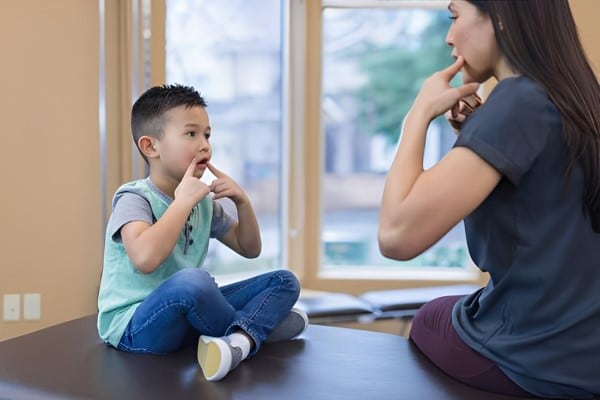 Speech or Language Delays in New York A Young Boy Sitting on a Therapy Table, Engaging in a Speech or Language Exercise with a woman